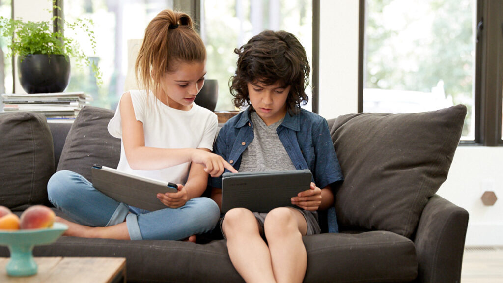 Two children sitting on couch with tablets